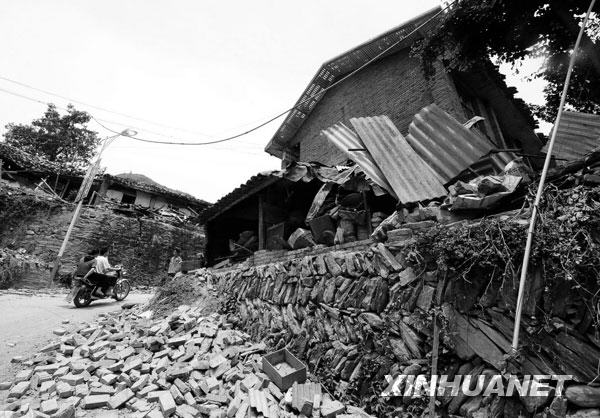 2008年5月15日，当地群众从甘肃省陇南市文县碧口地区三乡一镇地震灾区一处被震毁的房屋旁走过。
