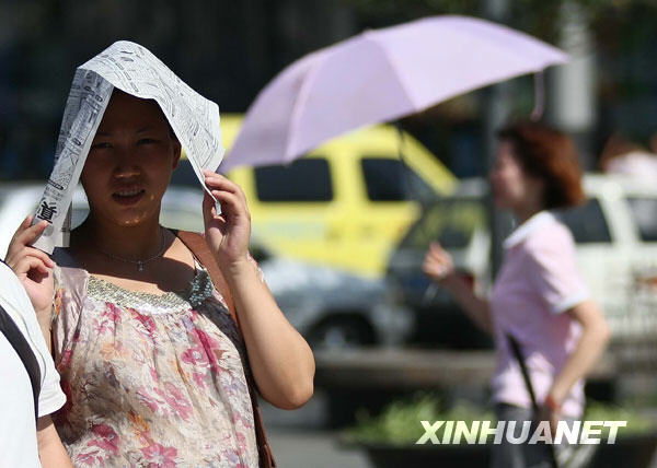 6月24日，一名郑州市民在街头用报纸遮挡烈日。